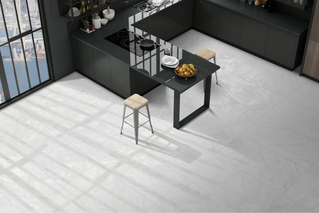 Modern kitchen with dark cabinetry and a glass-topped island. Two wooden stools are placed at the island, where a bowl of fruit sits. The white-tiled floor adds elegance, while large windows allow natural light to illuminate the sleek space, showcasing top-notch construction.