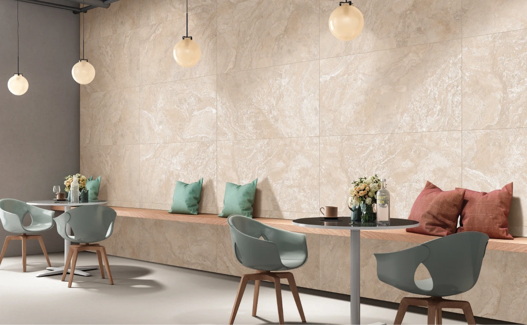 A modern cafe interior with light beige stone walls and round pendant lights offers a serene escape like a gentle stream. Small round tables with teal chairs accompany a wooden bench adorned with decorative pillows. Vases with flowers are artfully placed, creating an immaculate and inviting space.